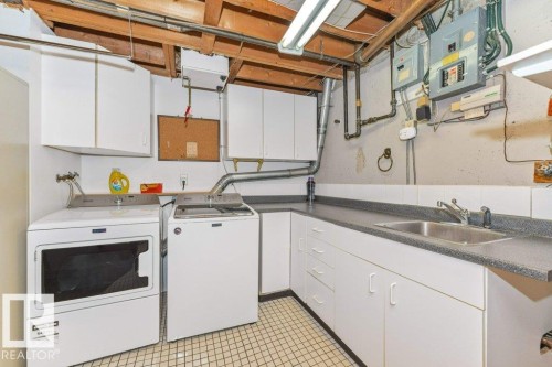 Laundry area featuring a utility sink, white base cabinetry with a dark countertop, white upper cabinetry, and a tiled floor - 11415 56 Avenue Nw, Edmonton, AB 