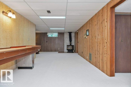 Expansive recreation space featuring wood-paneled walls, drop ceiling with integrated lighting, and a freestanding wood-burning stove - 11415 56 Avenue Nw, Edmonton, AB 