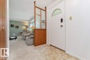 Entryway featuring a decorative transom window above the door, a wood-finish room divider with reeded glass panels, and carpeting - 11415 56 Avenue Nw, Edmonton, AB 