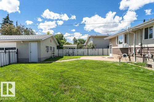 Expansive backyard featuring a large green lawn, concrete patio, and a detached garage with a white roll-up door - 11415 56 Avenue Nw, Edmonton, AB 