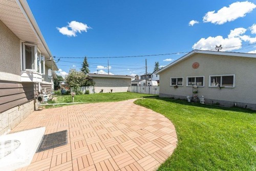 Expansive rear yard featuring a curved paver patio, manicured lawn, and a light-colored stucco exterior with multiple windows - 11415 56 Avenue Nw, Edmonton, AB 
