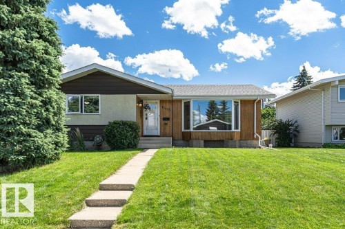 Split-level residence featuring a prominent bay window, stucco and wood siding, a concrete walkway with steps, mature front landscaping, and an expansive front lawn - 11415 56 Avenue Nw, Edmonton, AB 