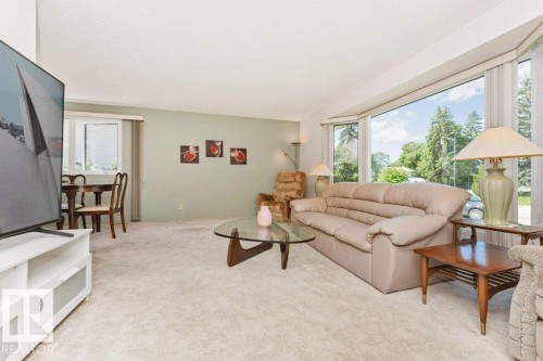 Living area featuring a large bay window, light-colored carpeting, and pale green wall accents - 11415 56 Avenue Nw, Edmonton, AB 