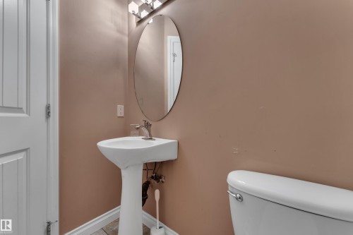 Pedestal sink with chrome faucet, oval mirror, and wall-mounted light fixture - 3455 29 Street Nw, Edmonton, AB 