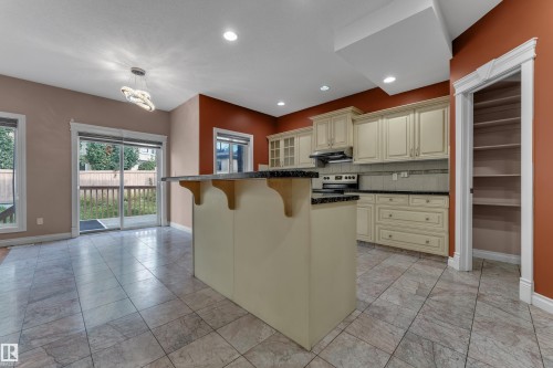 Kitchen featuring a central island with countertop, tile flooring, cream-finish cabinetry, built-in shelving, and sliding glass doors to an outdoor deck - 3455 29 Street Nw, Edmonton, AB 