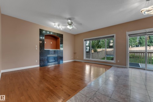 Hardwood flooring, tiled flooring, built-in fireplace with dark stone surround, large window, and glass sliding door - 3455 29 Street Nw, Edmonton, AB 
