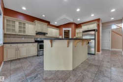 Kitchen featuring an island with a dark countertop, stainless steel appliances, cream cabinetry with glass-front uppers, and tiled flooring - 