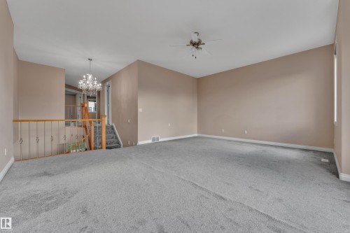 Spacious carpeted living area with vaulted ceilings, natural wood railing, chandelier, and ceiling fan - 3455 29 Street Nw, Edmonton, AB 