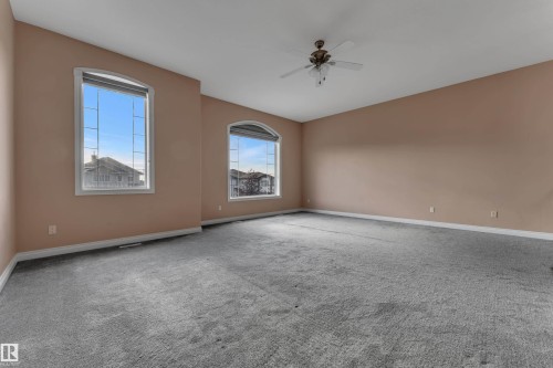 Expansive room featuring neutral-toned walls, gray carpeting, dual arched windows, and a ceiling fan - 3455 29 Street Nw, Edmonton, AB 