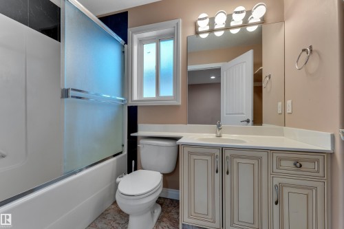 Bathroom featuring a built-in tub with a sliding glass enclosure, single vanity with a white countertop, wall-mounted mirror, and vanity light fixture - 3455 29 Street Nw, Edmonton, AB 