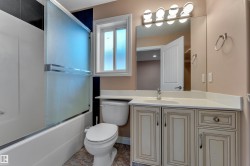 Bathroom featuring a built-in tub with a sliding glass enclosure, single vanity with a white countertop, wall-mounted mirror, and vanity light fixture - 