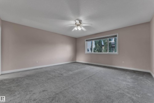 Spacious room with gray carpeting, ceiling fan, and a wide window with white trim - 3455 29 Street Nw, Edmonton, AB 