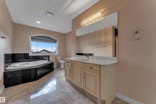 Soaking tub with black surround, single vanity with light countertop, large mirror with integrated lighting, and tile flooring - 3455 29 Street Nw, Edmonton, AB 