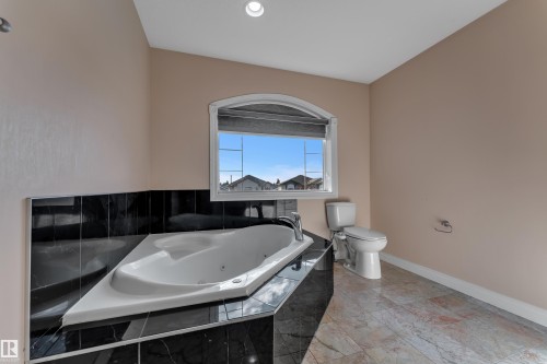 Corner jetted tub with black tile surround, arched window, and tiled flooring - 3455 29 Street Nw, Edmonton, AB 