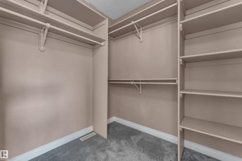 Custom closet system with multiple shelving units and hanging rods, complemented by gray carpeting - 3455 29 Street Nw, Edmonton, AB 