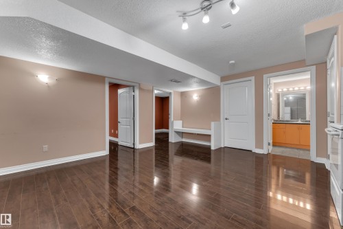 Wood-finish flooring, recessed lighting, and wall-mounted sconces illuminate this finished lower level, featuring a built-in bench and access to a bathroom with a vanity - 3455 29 Street Nw, Edmonton, AB 