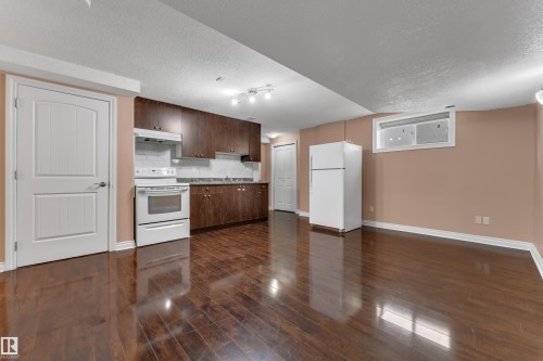 Full kitchen with dark wood-finish cabinetry, white appliances, and a tiled backsplash - 3455 29 Street Nw, Edmonton, AB 