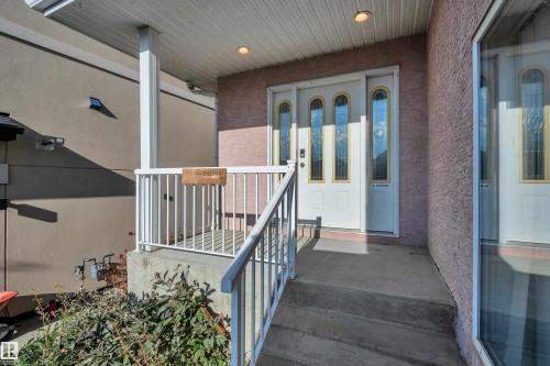 Covered concrete porch with white railing, glass-paneled entry door, and recessed lighting - 3455 29 Street Nw, Edmonton, AB 