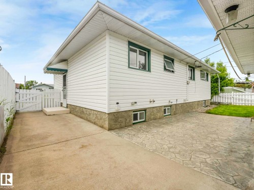 White vinyl siding, stone-finish foundation, stamped concrete patio, concrete pathway, and white picket fencing - 15916 88B Avenue Nw, Edmonton, AB 