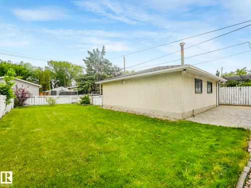 Expansive grassy yard with white picket fencing, a stucco exterior structure, and a paved driveway - 15916 88B Avenue Nw, Edmonton, AB 