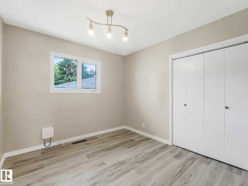 Light gray wall color, wood-finish flooring, white trim, white bi-fold closet doors, and a window with white casing - 15916 88B Avenue Nw, Edmonton, AB 