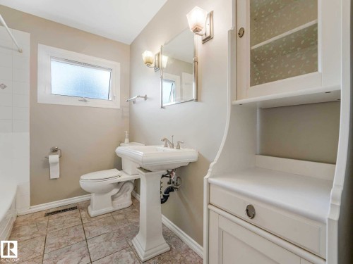 Pedestal sink with chrome fixtures, tiled flooring, built-in storage cabinet with glass-front upper, and a window with frosted glass - 15916 88B Avenue Nw, Edmonton, AB 