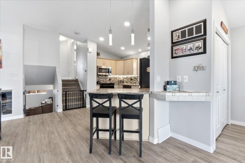 Open-concept living space with wood-finish flooring, a kitchen island with seating, recessed lighting, a built-in desk, and a staircase with carpeting - 2109 37 Avenue Nw, Edmonton, AB 