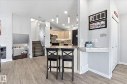 Open-concept living space with wood-finish flooring, a kitchen island with seating, recessed lighting, a built-in desk, and a staircase with carpeting - 