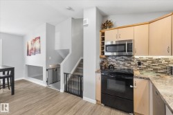 Kitchen featuring light wood-finish cabinetry, stainless steel microwave, black electric range, and mosaic tile backsplash - 