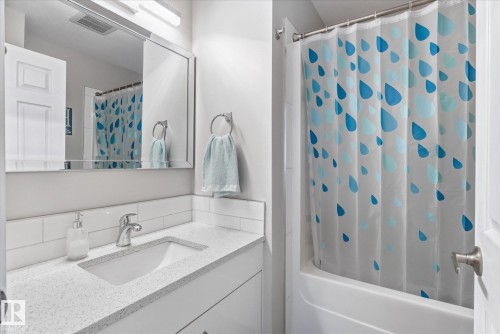 White paneled vanity with an integrated rectangular sink, speckled countertop, and white subway tile backsplash - 2109 37 Avenue Nw, Edmonton, AB 