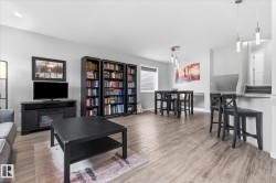 Open-concept living space with wood-finish flooring, built-in shelving, and a dining area featuring pendant lighting - 