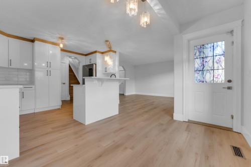 Wood-finish flooring, white kitchen cabinetry with gold accents, white subway tile backsplash, kitchen island with counter seating, and a front entry door with decorative glass - 3003 25 Avenue Nw, Edmonton, AB 