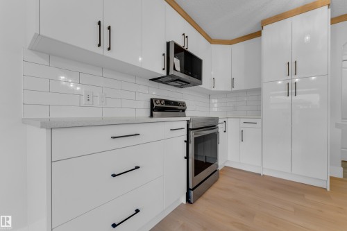 White cabinetry with black hardware, subway tile backsplash, stainless steel appliances, light wood-finish flooring, and light-toned countertops - 3003 25 Avenue Nw, Edmonton, AB 