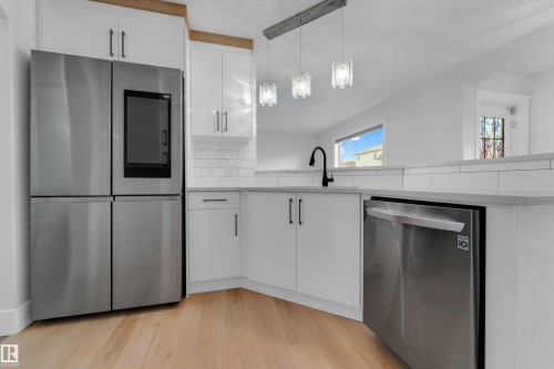 White cabinetry with matte black hardware, stainless steel appliances, wood-finish flooring, undermount sink with a matte black faucet, and pendant lighting fixtures - 3003 25 Avenue Nw, Edmonton, AB 