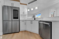 White cabinetry with matte black hardware, stainless steel appliances, wood-finish flooring, undermount sink with a matte black faucet, and pendant lighting fixtures - 