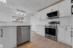 Kitchen featuring white cabinetry, stainless steel appliances, wood-finish flooring, white subway tile backsplash, and light-toned countertops - 