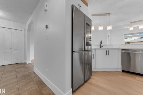 Stainless steel French door refrigerator, white kitchen cabinetry with black hardware, integrated stainless steel dishwasher, wood-finish flooring, and pendant lighting fixtures - 3003 25 Avenue Nw, Edmonton, AB 
