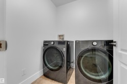 Dedicated laundry space featuring a white painted wall finish, light-toned flooring, and a contemporary door with a silver-finish handle - 