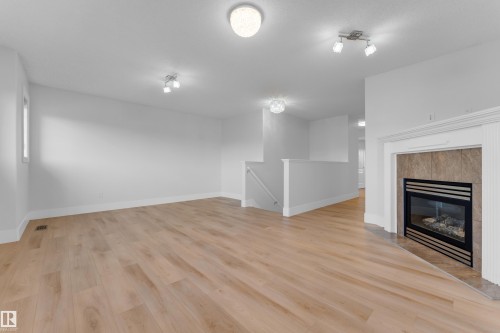 Spacious room featuring wood-finish flooring, a contemporary fireplace with a tiled surround, and crisp white walls - 3003 25 Avenue Nw, Edmonton, AB 