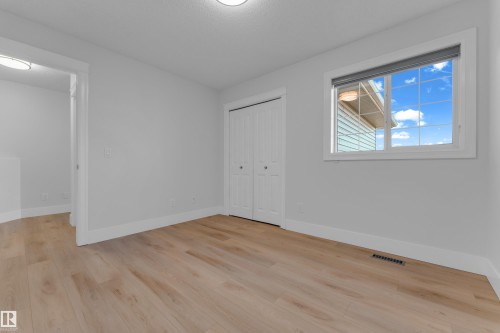 Light wood-finish flooring, white bi-fold closet doors, white trim, and a window with blinds - 3003 25 Avenue Nw, Edmonton, AB 