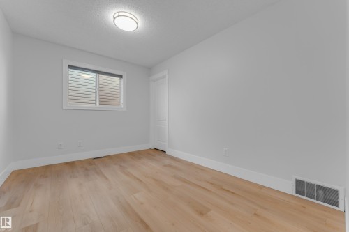 Bright, light-filled bedroom showcasing pristine wood-finish flooring, clean white walls, and abundant natural light from a transom window - 3003 25 Avenue Nw, Edmonton, AB 