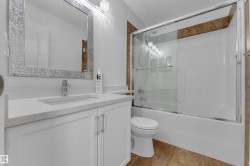 White vanity with an integrated sink and chrome faucet, mosaic-framed mirror, and a tub-shower combination with a sliding glass enclosure - 