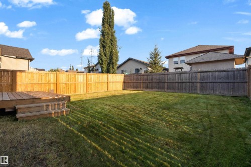 Expansive fenced backyard featuring a wood deck with steps, a manicured lawn, and mature trees - 3003 25 Avenue Nw, Edmonton, AB 