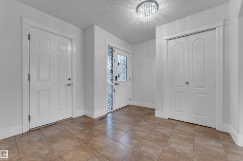 Tiled flooring entrance featuring a decorative crystal flush mount light, a paneled door, a paneled bi-fold door, and an exterior door with decorative glass - 3003 25 Avenue Nw, Edmonton, AB 