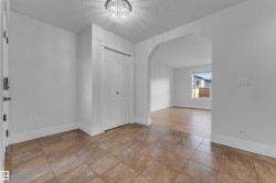 Tiled entryway flooring, crystal flush-mount ceiling light, white bi-fold closet doors, arched doorway, and wood-finish flooring - 