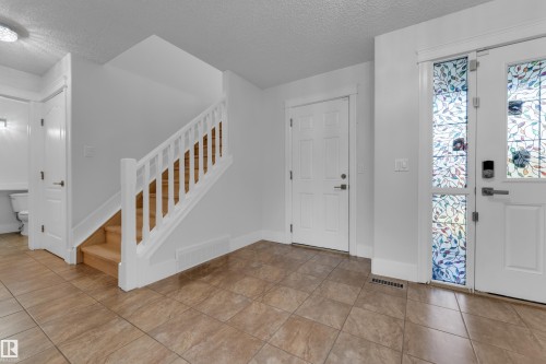 Tile flooring, white painted walls, wood staircase with white railing, and an entry door with decorative glass inserts - 3003 25 Avenue Nw, Edmonton, AB 
