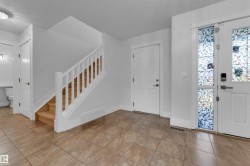 Tile flooring, white painted walls, wood staircase with white railing, and an entry door with decorative glass inserts - 