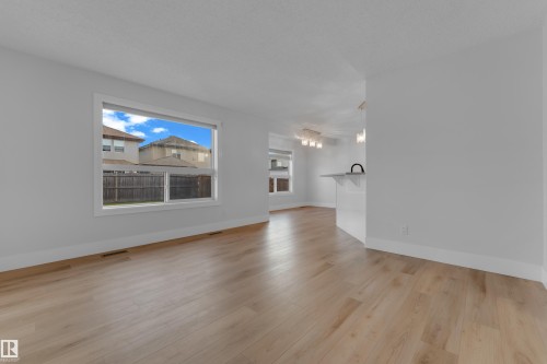 Light wood-finish flooring throughout, a large window, white walls, and a kitchen island with a black faucet - 3003 25 Avenue Nw, Edmonton, AB 