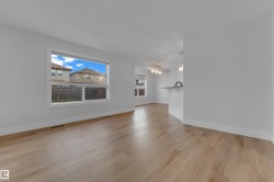 Light wood-finish flooring throughout, a large window, white walls, and a kitchen island with a black faucet - 