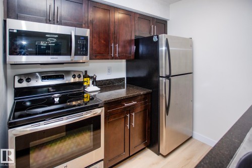 Stainless steel appliances, wood-finish cabinetry, dark countertops, built-in microwave, and wood-finish flooring - #201 1070 Mcconachie Bv Nw, Edmonton, AB 